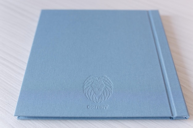 Closed photobook on white wooden table Blue textile wedding album with silver embossing