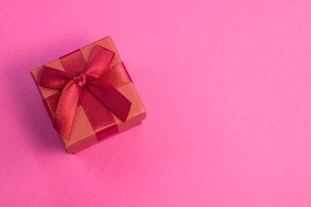 밝은 분홍색 배경에 실크 리본 활이 있는 닫힌 빨간색 선물 상자