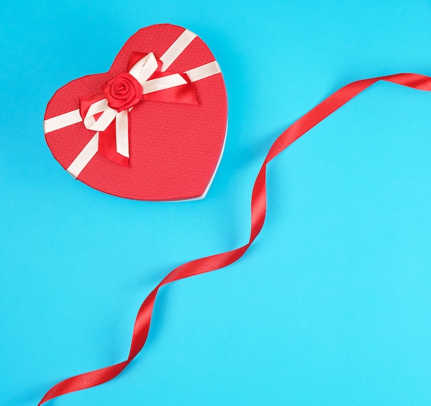 Closed red heart-shaped gift box with a bow on blue