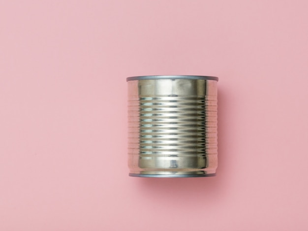 Closed tin can and fork on a pink background. Universal container for canning.