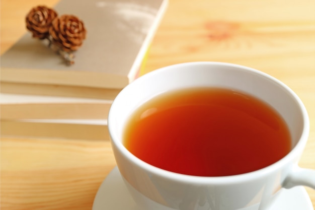 Closed up a cup of hot tea on wooden table with blurred stack of books and dry pine cones 