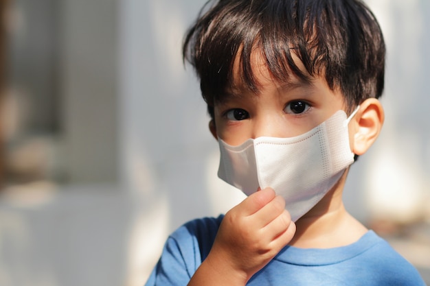 マスクを身に着けている子供のヘッドショットで引けた。コロナウイルスの発生と午後2.5危機の概念でアジアの少年。