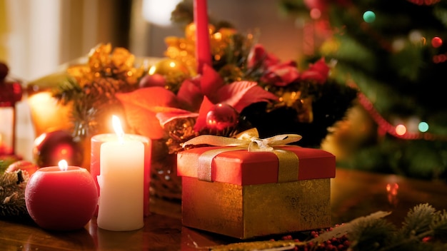 写真 輝くクリスマスライトと花輪に対して木製のテーブルでクリスマスプレゼントと燃えるろうそくのクローズアップ4k映像。冬のお祝いや休日にぴったりのショット
