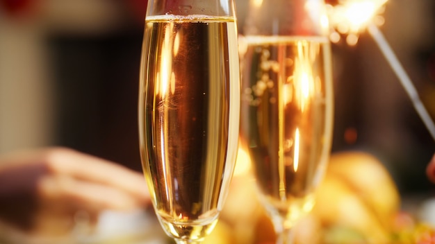 Closeup 4k footage of romantic couple holding sparkler next to glasses of fizzy champagne. Family celebrating Christmas and New Year holidays