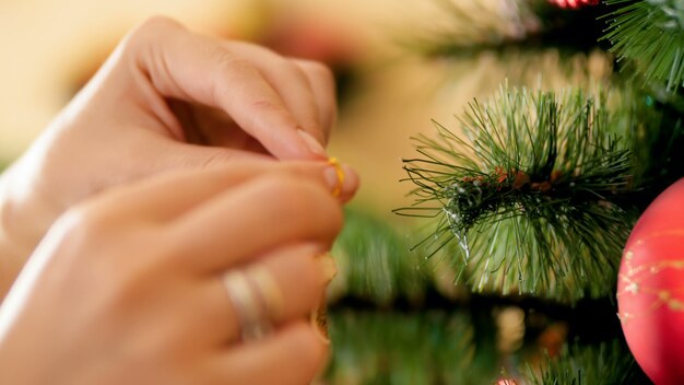 Closeup 4k footage of young woman putting decorative ornate star on Christmas tree branch. Family preparing and decorating house on winter holidays and celebrations.