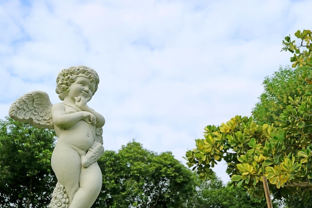 Closeup an adorable cupid sculpture in the garden against fluffy cloudy sky