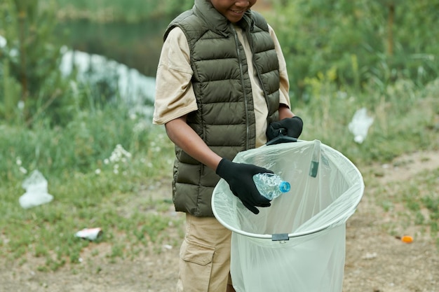 Photo closeup of african american boy picking up garbage in bag outdoors