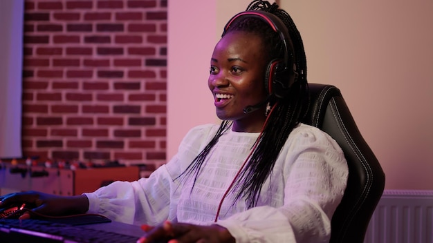 Closeup of african american gamer girl with gaming headset\
talking to team members in tournament on professional pc setup.\
woman looking at computer screen while playing multiplayer online\
game.