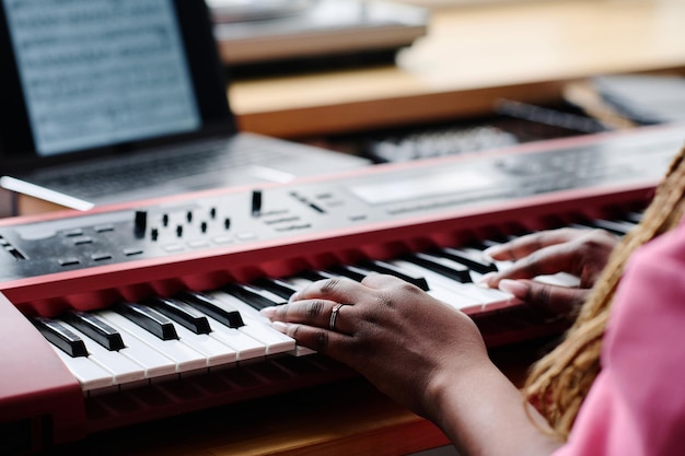 Closeup of african american girl using sheet music and learning to play synthesizer at table