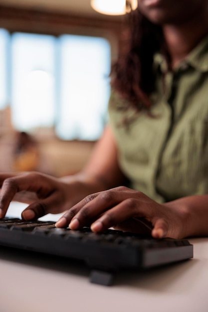 Closeup of african american student writing homework using computer keyboard while studying remote from home living room. Selective focus on woman freelancer hands typing text while chatting.