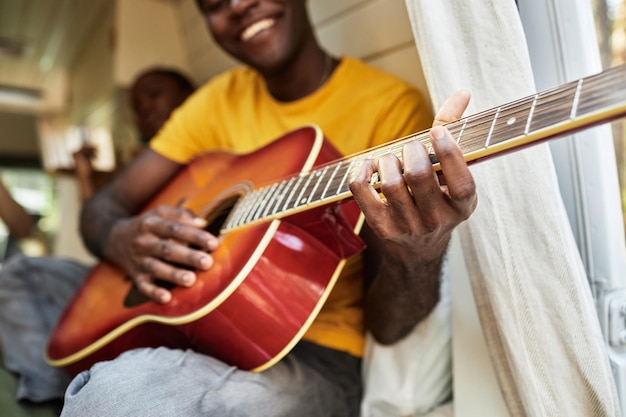 Closeup of african young man playing guitar sitting in van with his friends