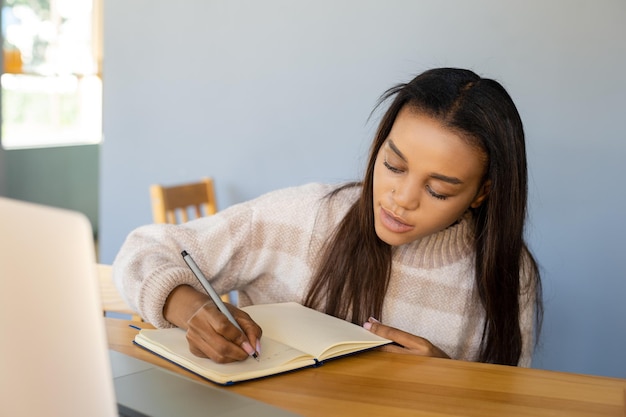 Closeup of an AfricanAmerican girl with a laptop taking important notes in a workbook