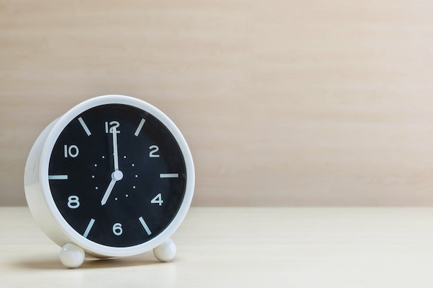 Closeup alarm clock for decorate in 7 o'clock on wood desk and wall background