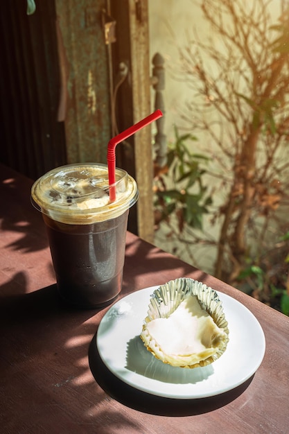 Closeup of Americano ice coffee or black coffee in cup mug and Coconut Cake in wood desk office desk in coffee shop at the cafe in gardenduring business work concept