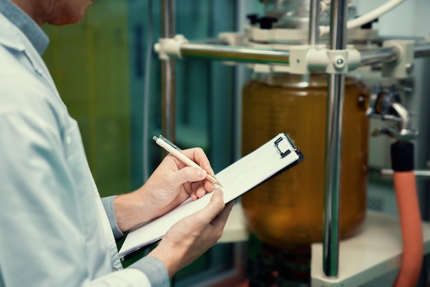 Closeup apothecary scientist recording data from CBD oil extractor in laboratory