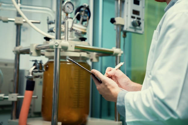 Closeup apothecary scientist recording data from CBD oil extractor in laboratory