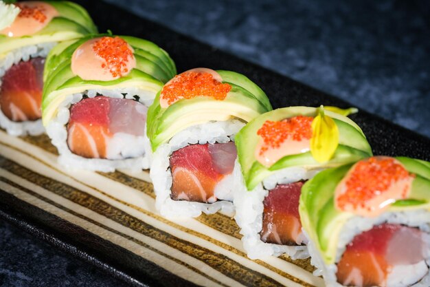 Closeup of appetizing tobiko roe with fresh green avocado slices on top of uramaki sushi rolls served on tray on marble counter