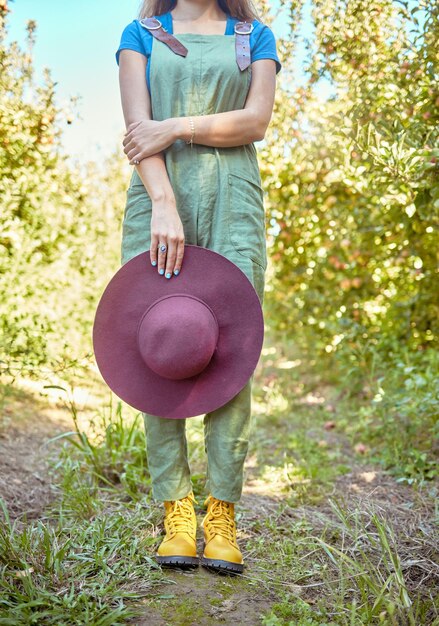 Closeup apple farmer standing alone on a farm and holding her sun hat Woman in dungarees surrounded by fresh agricultural fruit trees produce for harvest on remote sustainable apple orchard