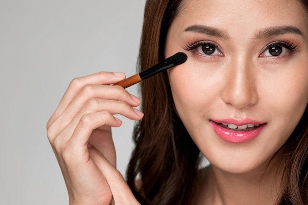 Closeup ardent female model applying her eyeshadow and holding a mirror