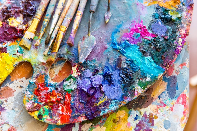 Foto primo piano della tavolozza d'arte con vernici miste colorate luminose, pennelli e spatole