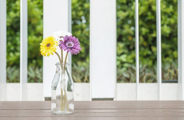 Крупный план искусственного красочного цветка на прозрачной стеклянной бутылке на деревянном стуле на предпосылке вида на сад