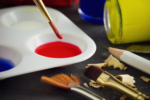 Closeup artist paint brush above color plate and poster color bottle on table