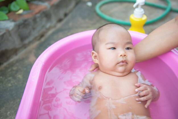 Closeup asian baby take a shower on daylight in pink Basin