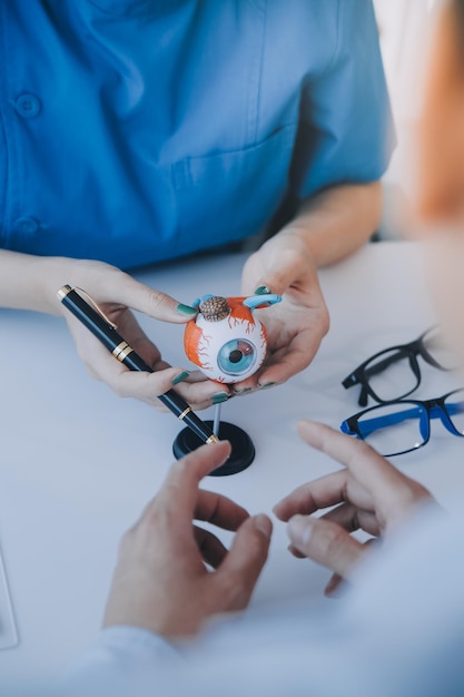 Foto closeup di una dottoressa asiatica che parla con un paziente anziano mostrando il modello del bulbo oculare e spiegando la malattia oculare in ospedale