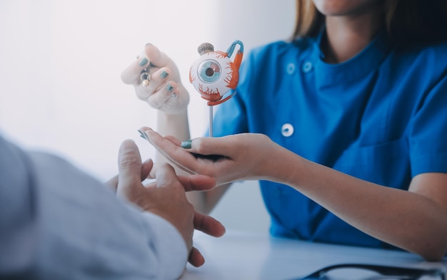 Closeup of Asian female doctor talking with elderly patient showing eyeball model and explaining eye disease in hospital