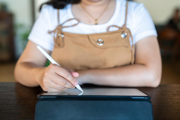 Closeup of asian freelance people business female wearing glasses stylish hipste Draw or taking note on digital tablet with electronic pen for browsing internet chatting and blogging in coffee shop