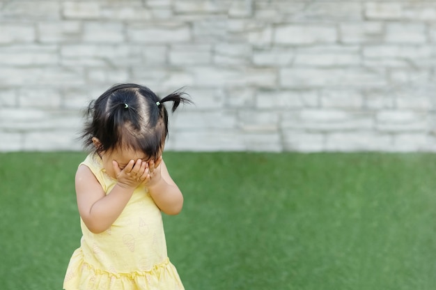 クローズアップアジアの女の子は顔から彼女の手を取り、草の床に誰かと隠れて遊ぶ