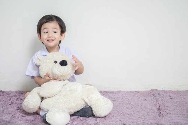 곰 인형으로 흥분된 얼굴로 근접 촬영 아시아 아이 카펫에 앉아