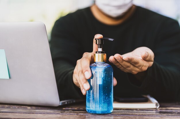 Primo piano uomo asiatico che fa disinfettante per le mani pompando gel alcolico prima di lavorare con un laptop tecnologico