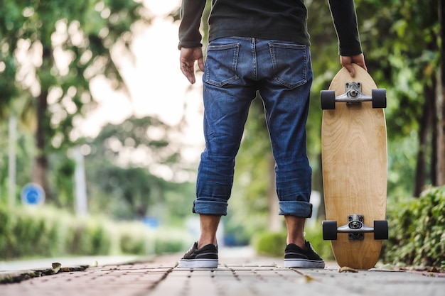 Uomo asiatico del primo piano che tiene surfskate o skateboard nel parco all'aperto