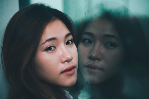 Крупный план азиатской грустной женщины у зеркала с отражением в дождливом дне