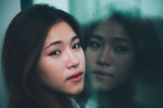 Closeup asian sad woman at mirror with reflection in a raining day vintage styleheartbreak woman conceptstress girl