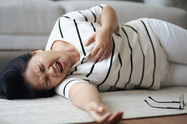 집에서 혼자 바닥에 누워 심장 마비를 겪고 있는 아시아 여성의 근접 촬영. 가슴을 만지고 가슴이 아픈 여자. 건강 관리 및 의료 개념입니다.