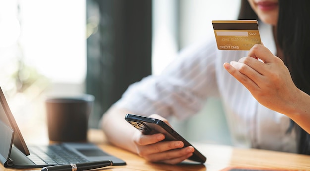 Closeup asian woman holding gold credit card and smartphone, sitting at home, happy satisfied young female customer shopping online, purchasing, making secure online payment.