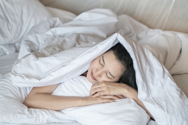 Sonno asiatico della donna del primo piano sul letto sotto la coperta in camera da letto