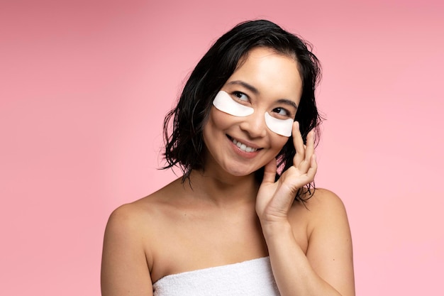 目の下にコラーゲン ハイドロゲルの目のパッチを適用する健康的な新鮮な肌を持つアジアの女性のクローズ アップ