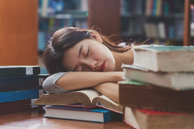 読んで、大学の図書館で様々な本と木製のテーブルで寝ているカジュアルなスーツでクローズアップアジアの若い学生