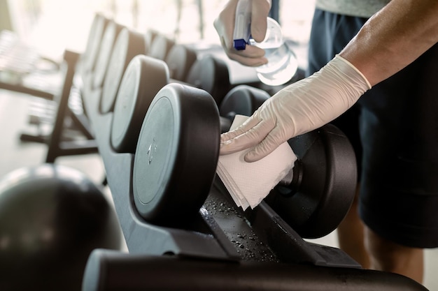 Closeup of athletic man cleaning dumbbells with disinfectant in a gym