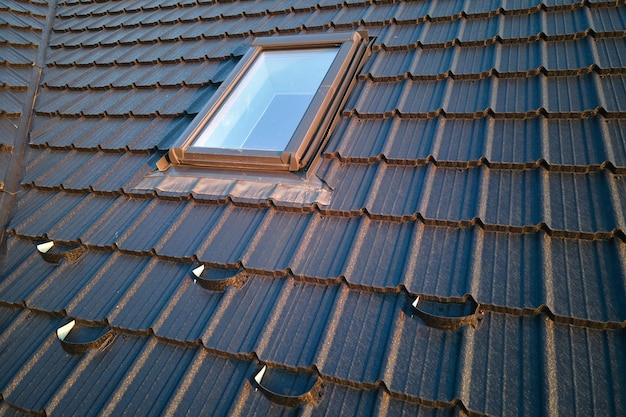 Closeup of attic window on house roof top covered with ceramic shingles Tiled covering of building