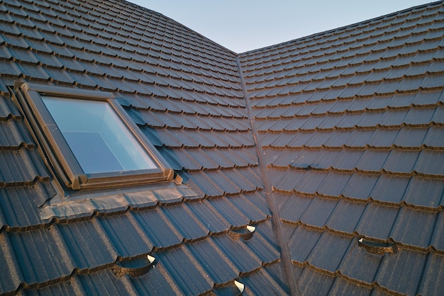 Closeup of attic window on house roof top covered with ceramic shingles Tiled covering of building