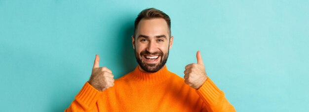 Photo closeup of attractive bearded man showing thumbup approve and like recommending product light blue b