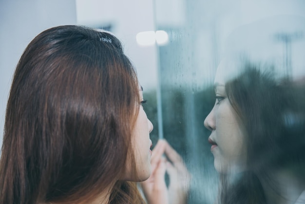 Closeup Aziatische vrouw verdrietig van liefde op spiegel met reflectie in een regenachtige dag vintage stijl liefdesverdriet vrouw conceptstress girl