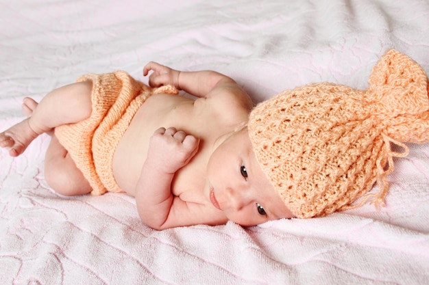 Closeup of a baby lying in a knitted hat and shorts