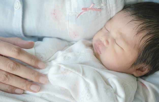 Closeup a baby sleeping comfortably in in the mother's arms