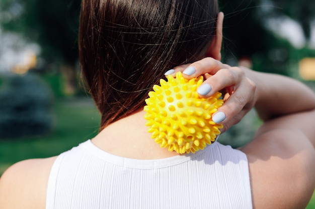 Closeup on back of young woman doing neck and shoulder massage with spiky rubber ball relaxing tense...