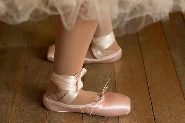 Foto primo piano dei piedi di una ballerina in scarpe da punta su un pavimento di legno